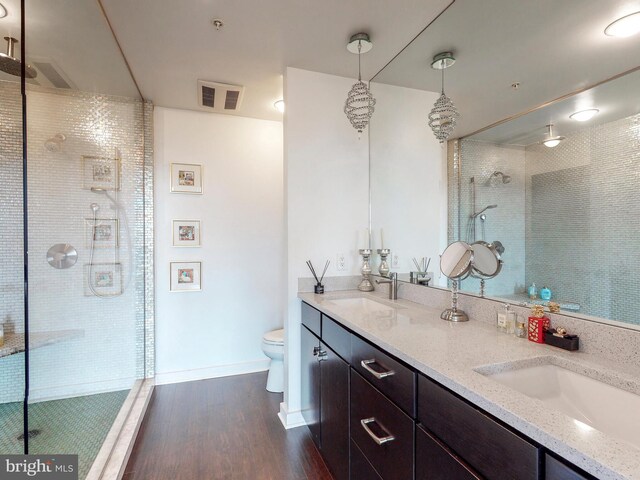 bathroom with tiled shower, vanity, hardwood / wood-style flooring, and toilet