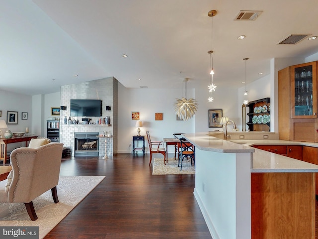 kitchen with light stone countertops, a brick fireplace, sink, decorative light fixtures, and dark hardwood / wood-style floors