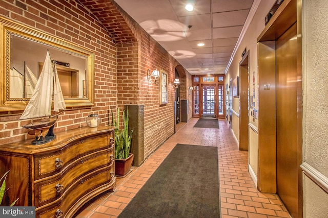 hall featuring brick floor, elevator, a drop ceiling, and brick wall