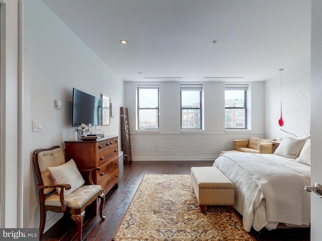 bedroom with dark hardwood / wood-style floors and brick wall