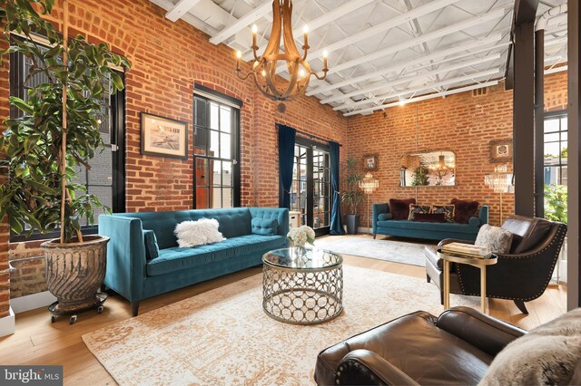 interior space featuring a notable chandelier, light hardwood / wood-style flooring, a towering ceiling, brick wall, and beam ceiling