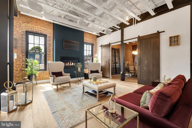 living room featuring brick wall, a barn door, light wood-type flooring, and a towering ceiling