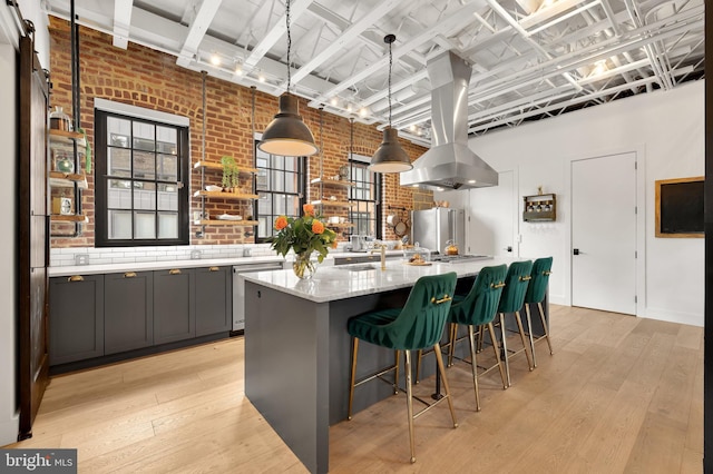 kitchen with light wood-type flooring, a large island with sink, decorative light fixtures, a breakfast bar, and brick wall