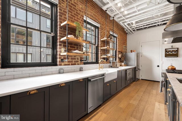 kitchen featuring a high ceiling, sink, appliances with stainless steel finishes, brick wall, and light hardwood / wood-style floors