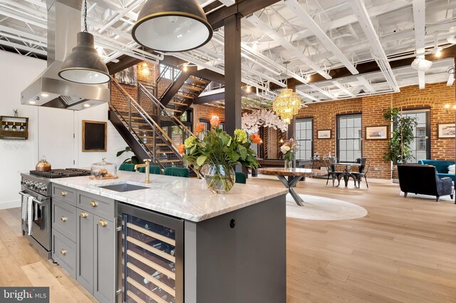 kitchen with range with two ovens, beverage cooler, light stone countertops, brick wall, and light hardwood / wood-style floors