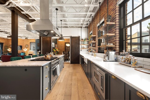 kitchen featuring hanging light fixtures, appliances with stainless steel finishes, light hardwood / wood-style floors, brick wall, and island range hood