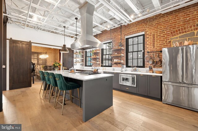 kitchen featuring brick wall, light hardwood / wood-style flooring, appliances with stainless steel finishes, a center island, and a barn door