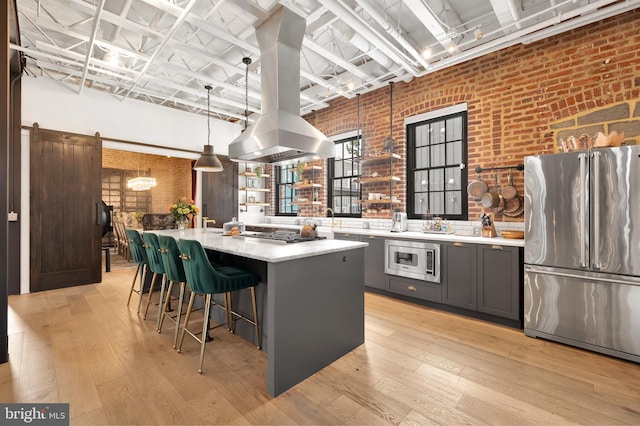 kitchen featuring a center island, a barn door, appliances with stainless steel finishes, brick wall, and light wood-type flooring