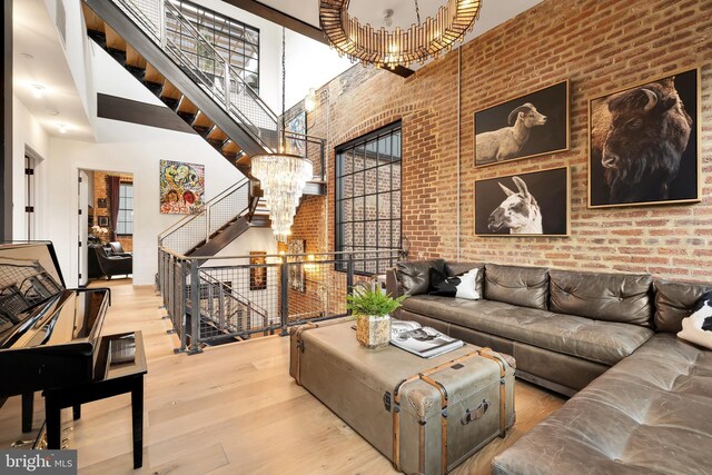 living room with brick wall, a high ceiling, a notable chandelier, and light wood-type flooring