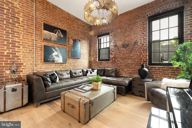 living area featuring a chandelier, brick wall, and light wood-type flooring