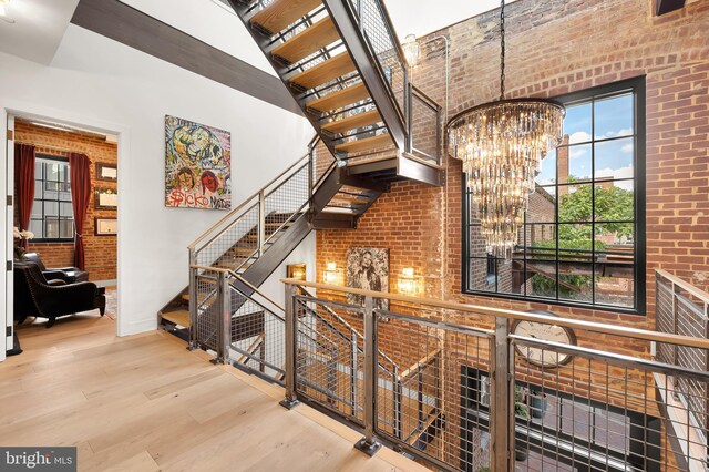 stairs with brick wall, a high ceiling, wood-type flooring, and a chandelier