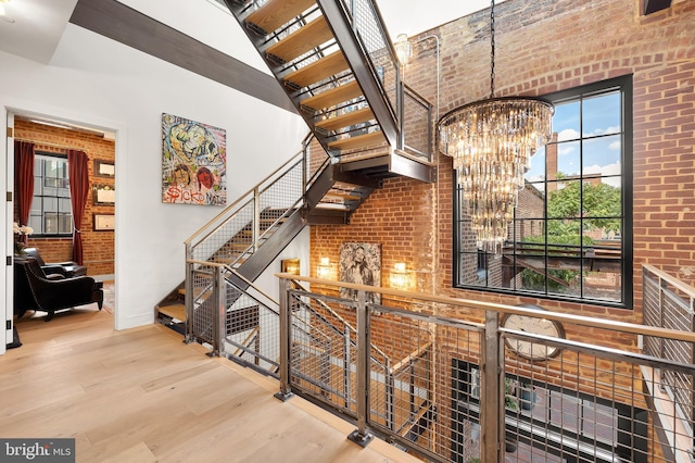 stairway featuring a high ceiling, a healthy amount of sunlight, wood finished floors, and an inviting chandelier