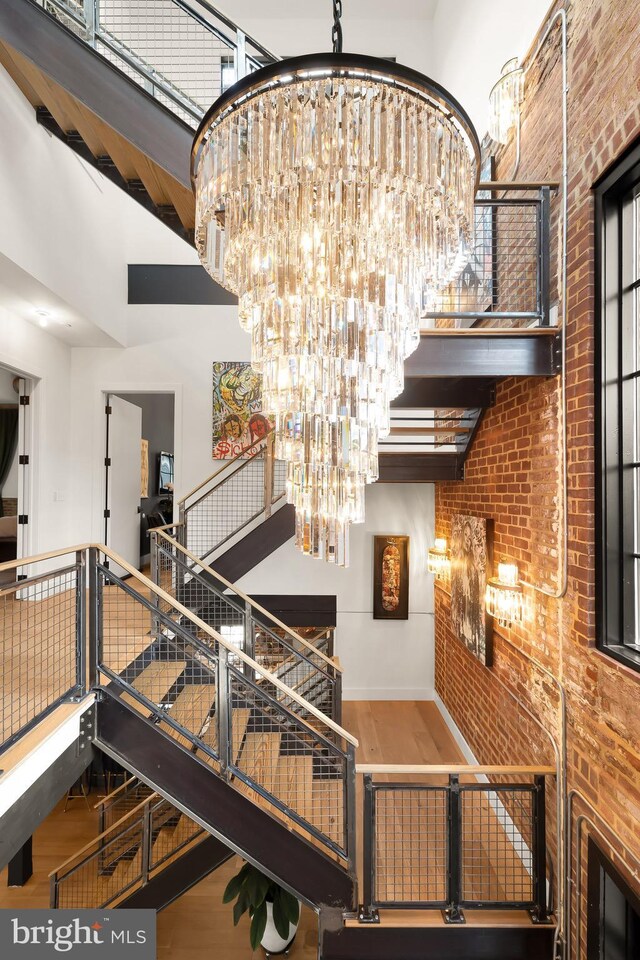 stairs with wood-type flooring, brick wall, an inviting chandelier, and a high ceiling