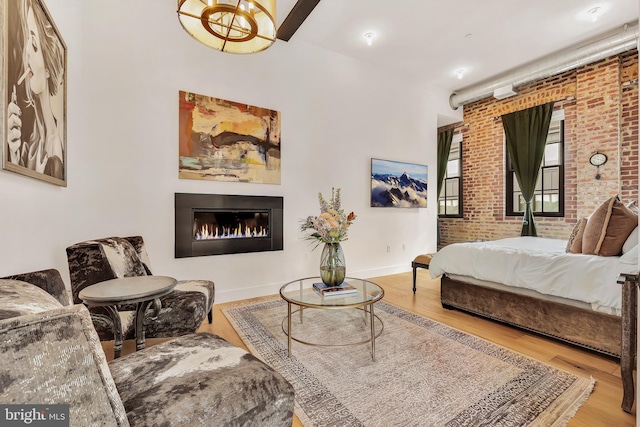 bedroom featuring brick wall, wood finished floors, a glass covered fireplace, and baseboards