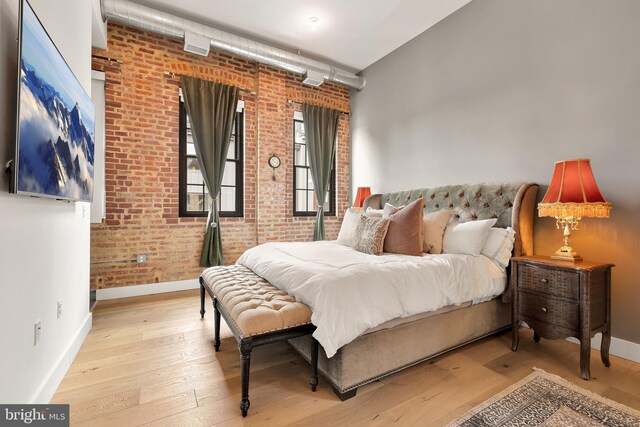 bedroom featuring brick wall and light hardwood / wood-style floors