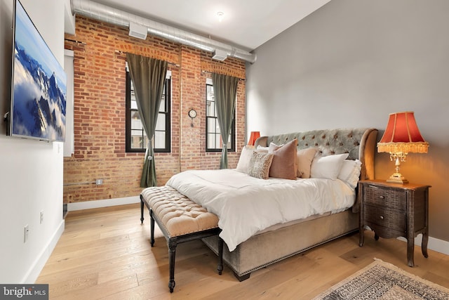 bedroom with wood-type flooring, baseboards, and brick wall