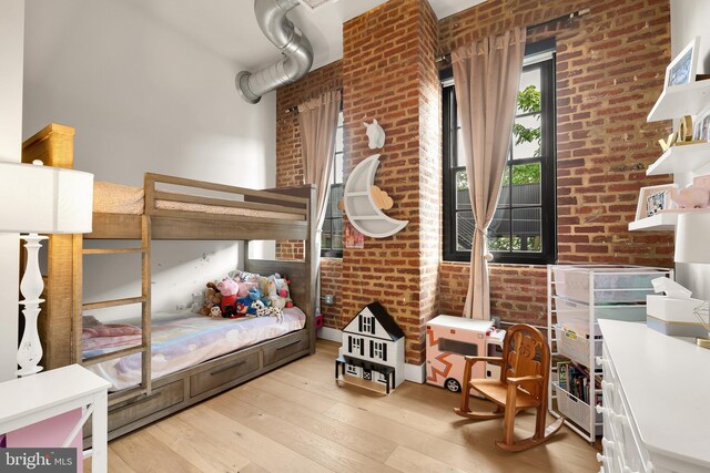 bedroom with brick wall and light hardwood / wood-style flooring