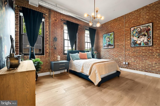 bedroom featuring baseboards, brick wall, hardwood / wood-style flooring, and a notable chandelier