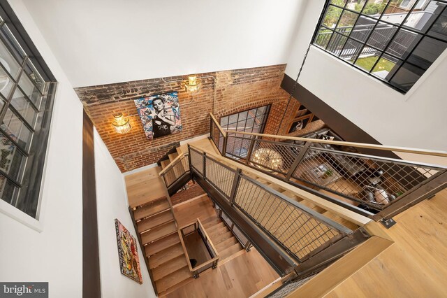 stairs with wood-type flooring, brick wall, and a high ceiling