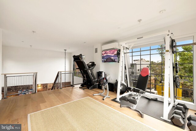 workout area with a wall unit AC and light hardwood / wood-style floors