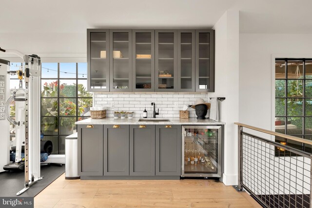 bar with light wood-type flooring, beverage cooler, sink, and gray cabinetry