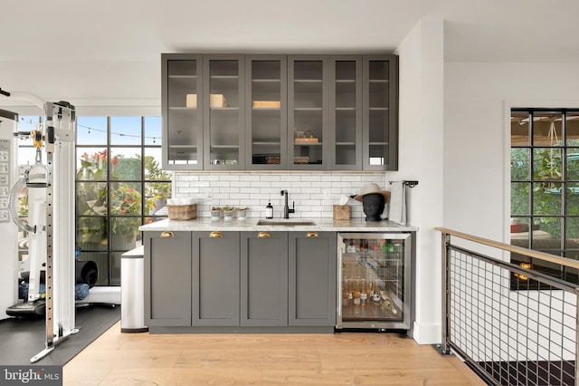 bar featuring tasteful backsplash, wine cooler, a sink, and light wood finished floors