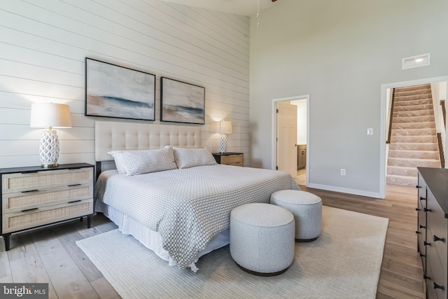 bedroom featuring visible vents, connected bathroom, baseboards, a towering ceiling, and wood finished floors