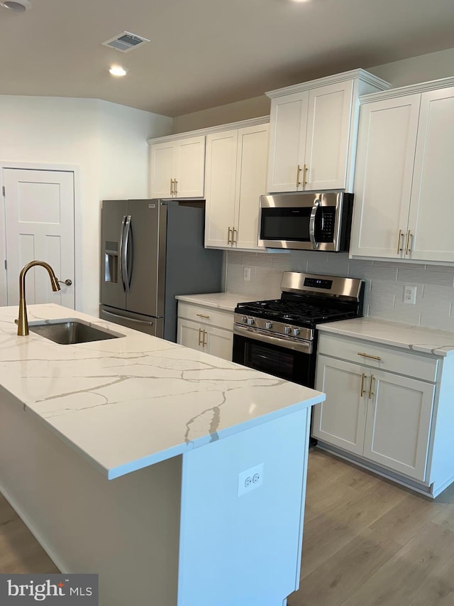 kitchen with visible vents, light wood-type flooring, a sink, tasteful backsplash, and appliances with stainless steel finishes