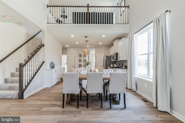 dining room featuring baseboards, light wood finished floors, recessed lighting, stairs, and a towering ceiling