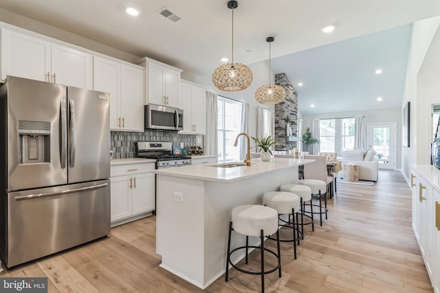 kitchen with light wood-style flooring, a sink, open floor plan, appliances with stainless steel finishes, and white cabinets