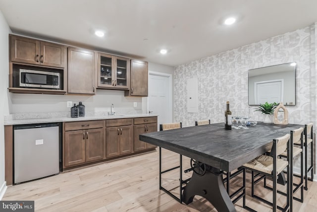 kitchen featuring wallpapered walls, a sink, fridge, stainless steel microwave, and light wood-type flooring