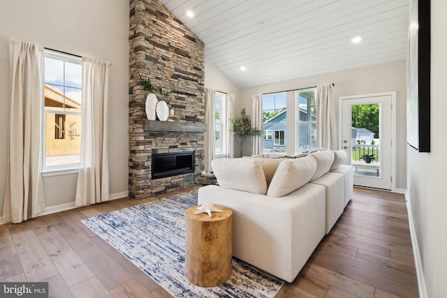 living room featuring high vaulted ceiling, hardwood / wood-style flooring, recessed lighting, a stone fireplace, and baseboards