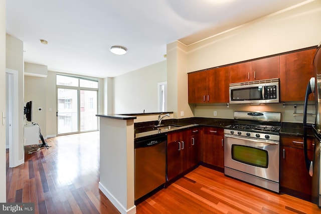 kitchen with dark stone countertops, hardwood / wood-style floors, a wall of windows, sink, and appliances with stainless steel finishes