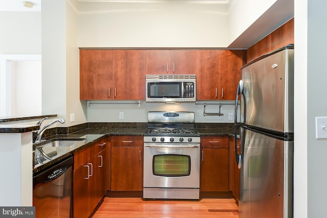 kitchen featuring light wood-type flooring, dark stone counters, stainless steel appliances, and sink