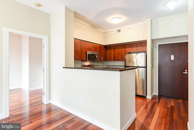 kitchen featuring dark stone countertops, stainless steel appliances, dark hardwood / wood-style floors, and kitchen peninsula