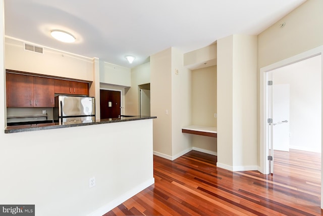 kitchen with dark wood-type flooring, stainless steel fridge, dark stone counters, and kitchen peninsula