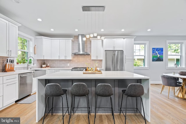 kitchen with stainless steel appliances, wall chimney range hood, a kitchen island, and light countertops