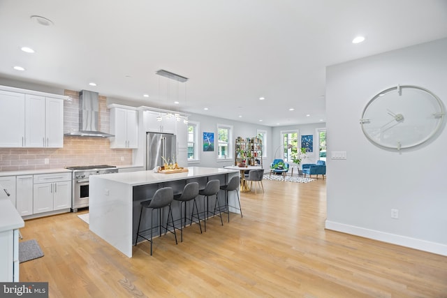 kitchen with premium appliances, white cabinets, light countertops, and wall chimney range hood