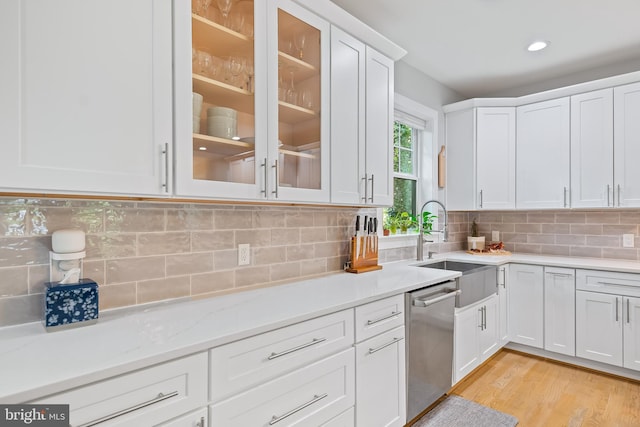 kitchen featuring white cabinets, glass insert cabinets, stainless steel dishwasher, light wood-style floors, and a sink