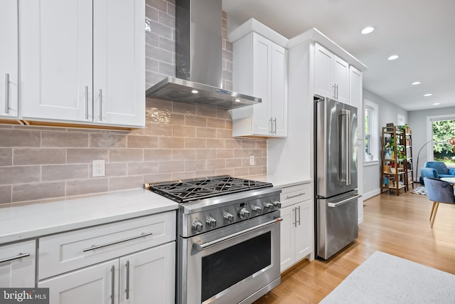 kitchen with premium appliances, white cabinets, light countertops, and wall chimney exhaust hood