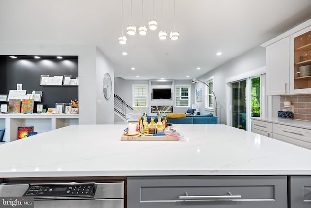 kitchen featuring white cabinets, a kitchen island, glass insert cabinets, open floor plan, and light stone counters