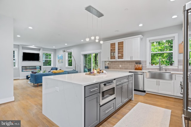 kitchen with white cabinets, glass insert cabinets, appliances with stainless steel finishes, light countertops, and a sink