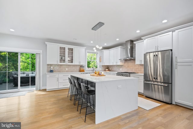 kitchen with pendant lighting, glass insert cabinets, a kitchen island, high quality fridge, and wall chimney exhaust hood