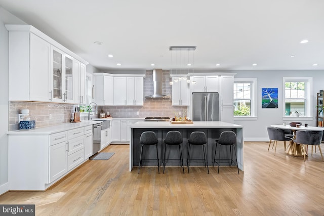 kitchen featuring wall chimney range hood, a kitchen island, appliances with stainless steel finishes, and light countertops