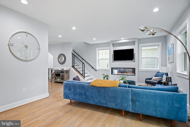 living room with stairs, a glass covered fireplace, light wood-style flooring, and recessed lighting