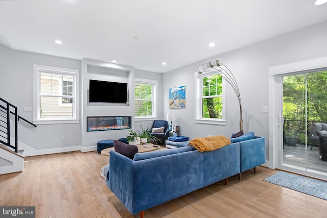 living room with light wood-style floors, recessed lighting, stairs, and a glass covered fireplace