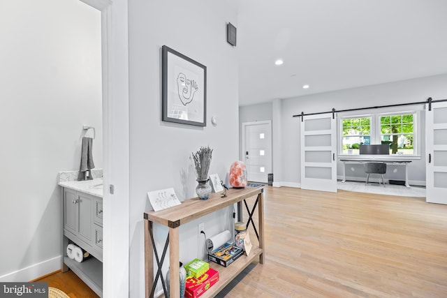 hall featuring recessed lighting, light wood-style flooring, baseboards, and a barn door