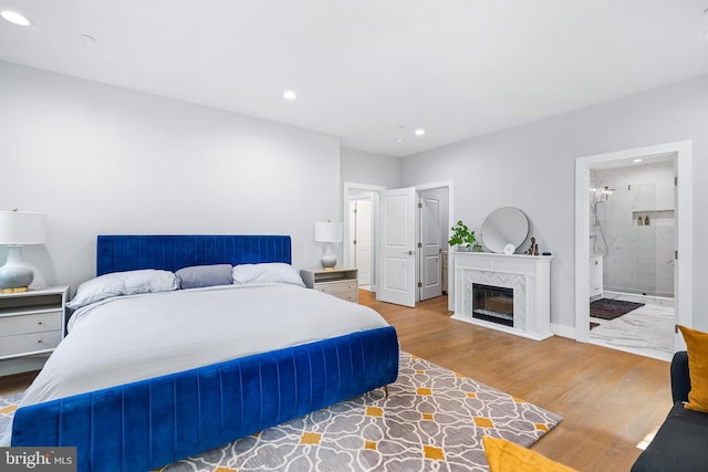 bedroom with a glass covered fireplace, baseboards, recessed lighting, and wood finished floors