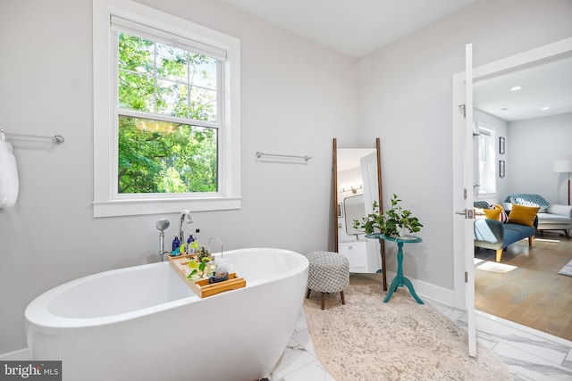 bathroom featuring a freestanding bath, marble finish floor, and baseboards