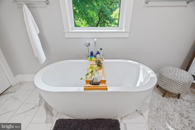 bathroom with marble finish floor, a freestanding bath, and baseboards